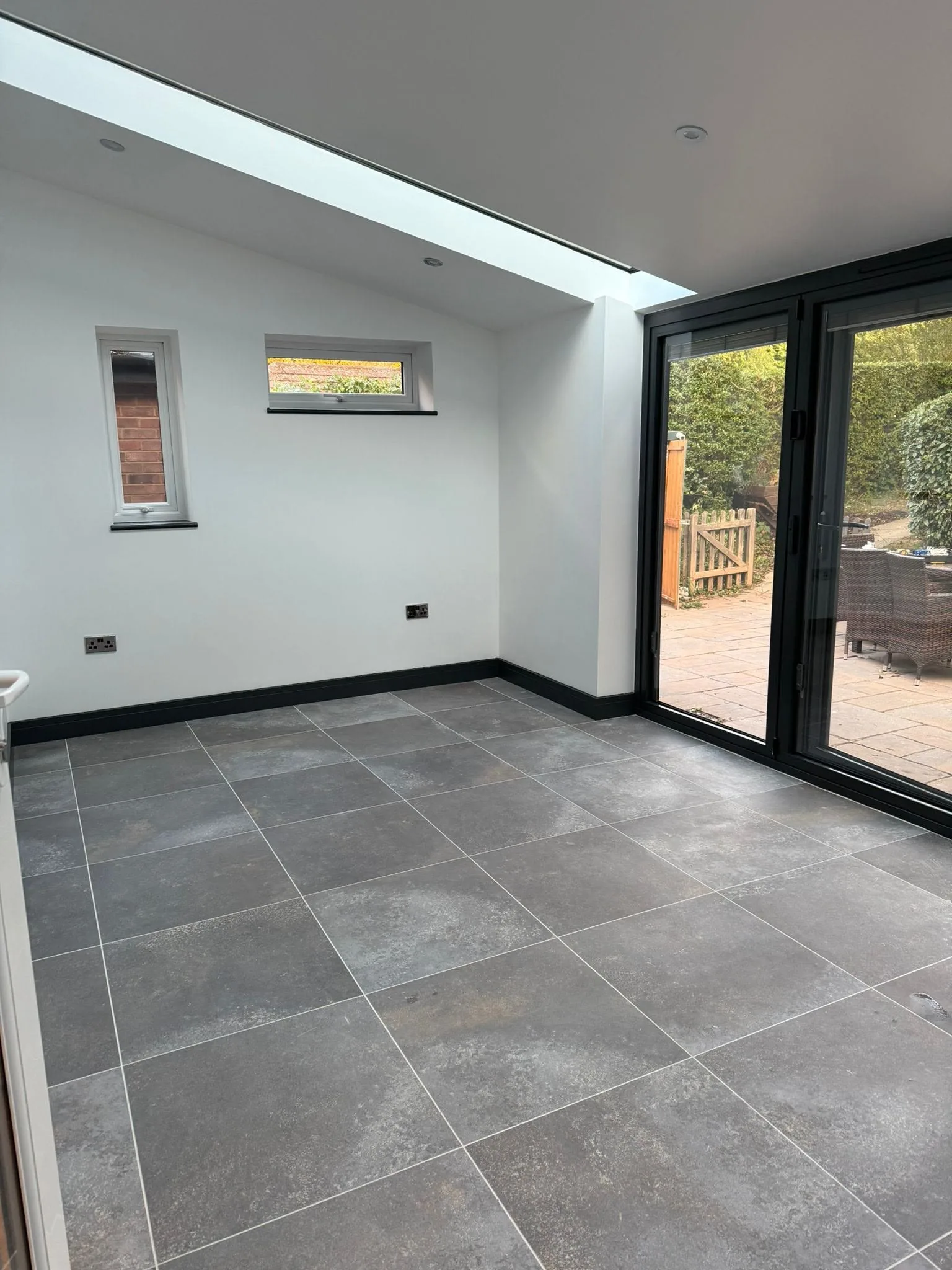 Finished conservatory interior with tiled floor, two glazed roof panels and dark bifold doors opening to the garden