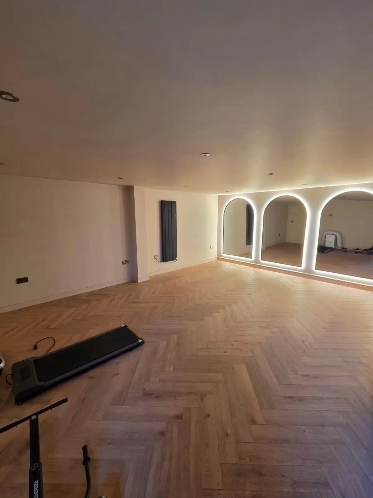Completed family gym with herringbone flooring, wall lighting and illuminated arched mirrors