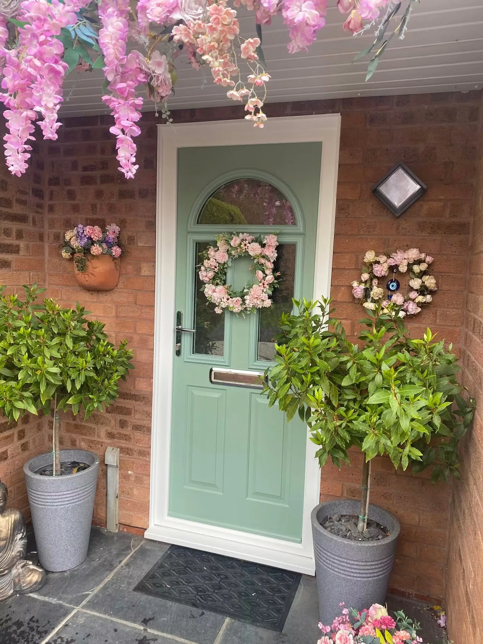 Green entrance door framed by flowers and potted plants